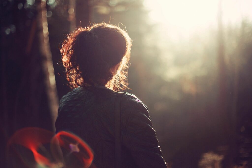 A woman standing in the sunlight near trees.